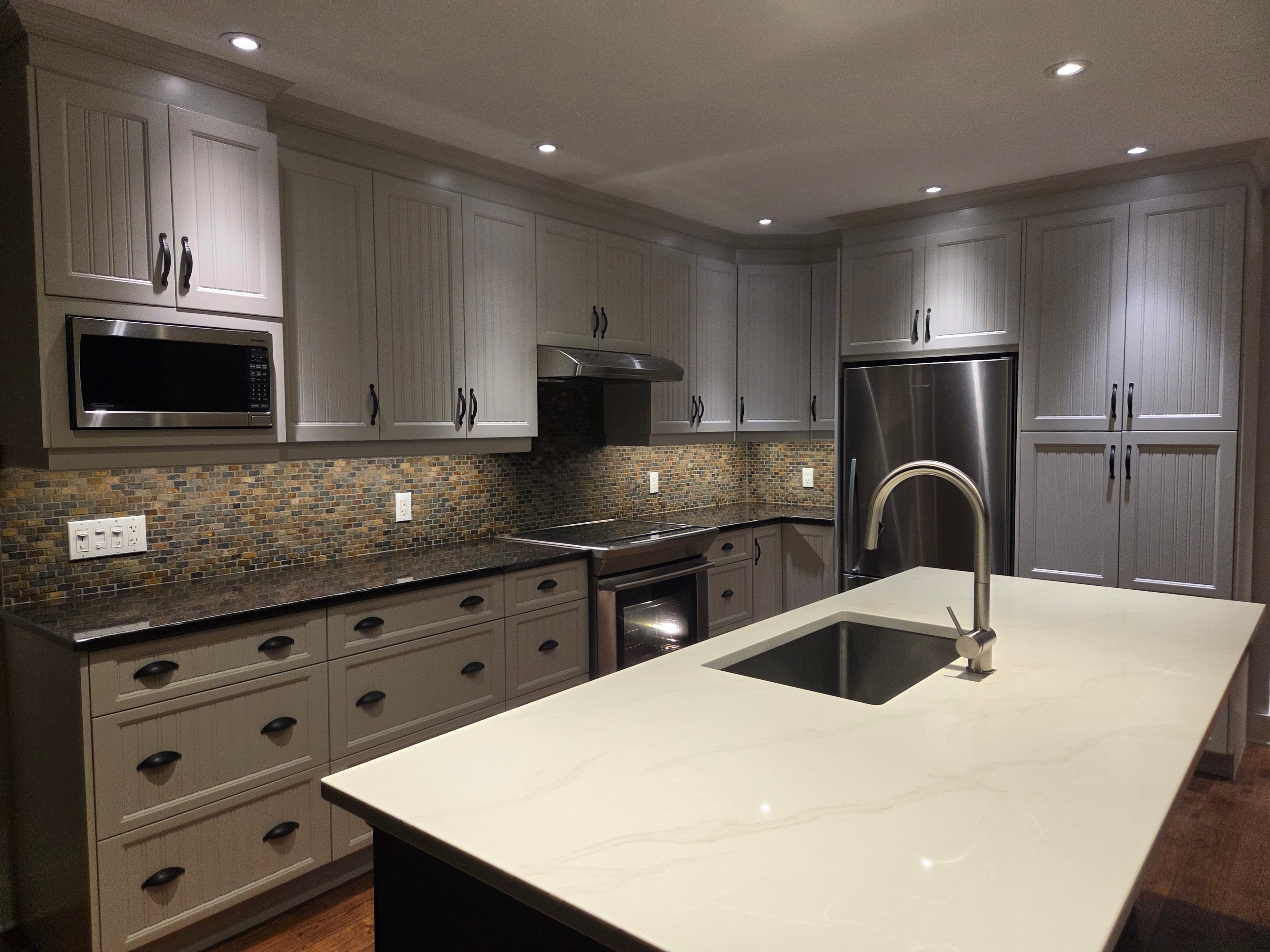 A finished kitchen in soft grey with black cup pulls, a mosaic stone backsplash and a white quartz island